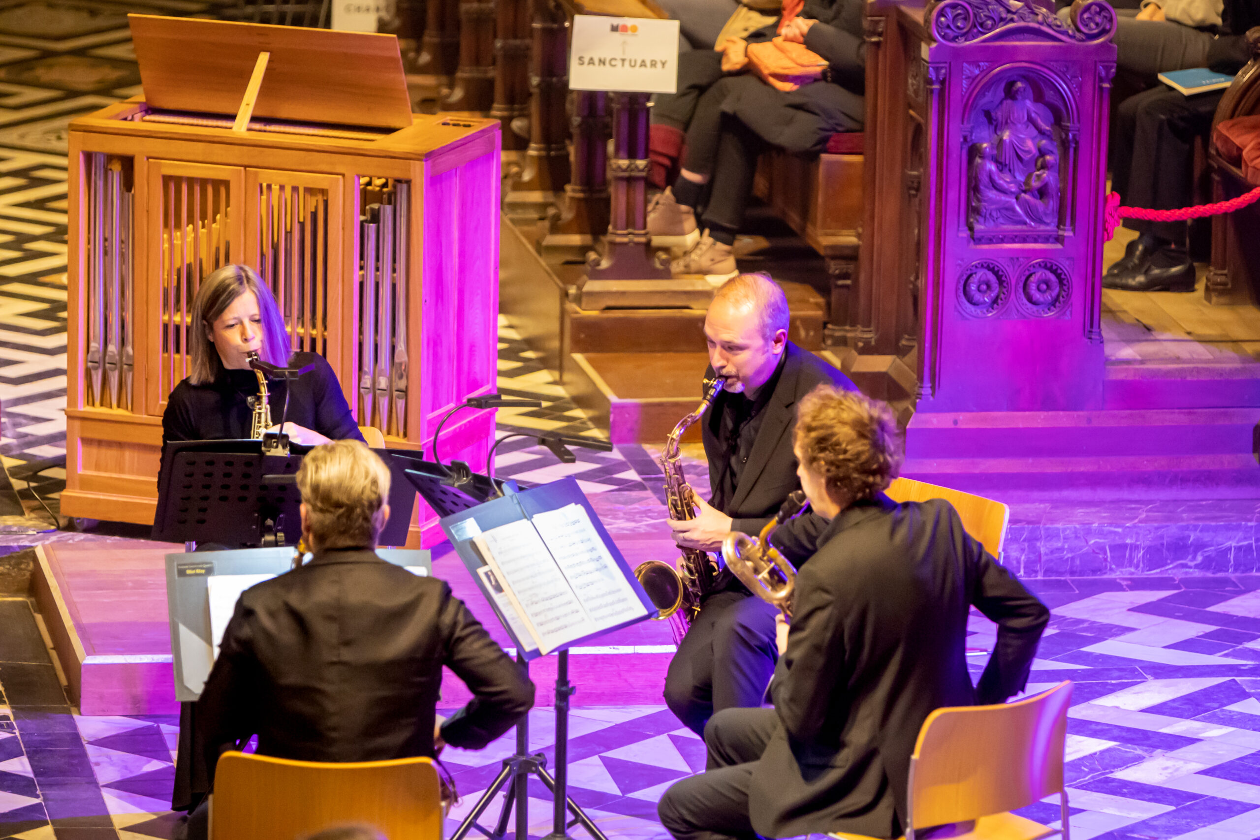 A close-up of a saxophone quartet perform, lit with pink lighting.