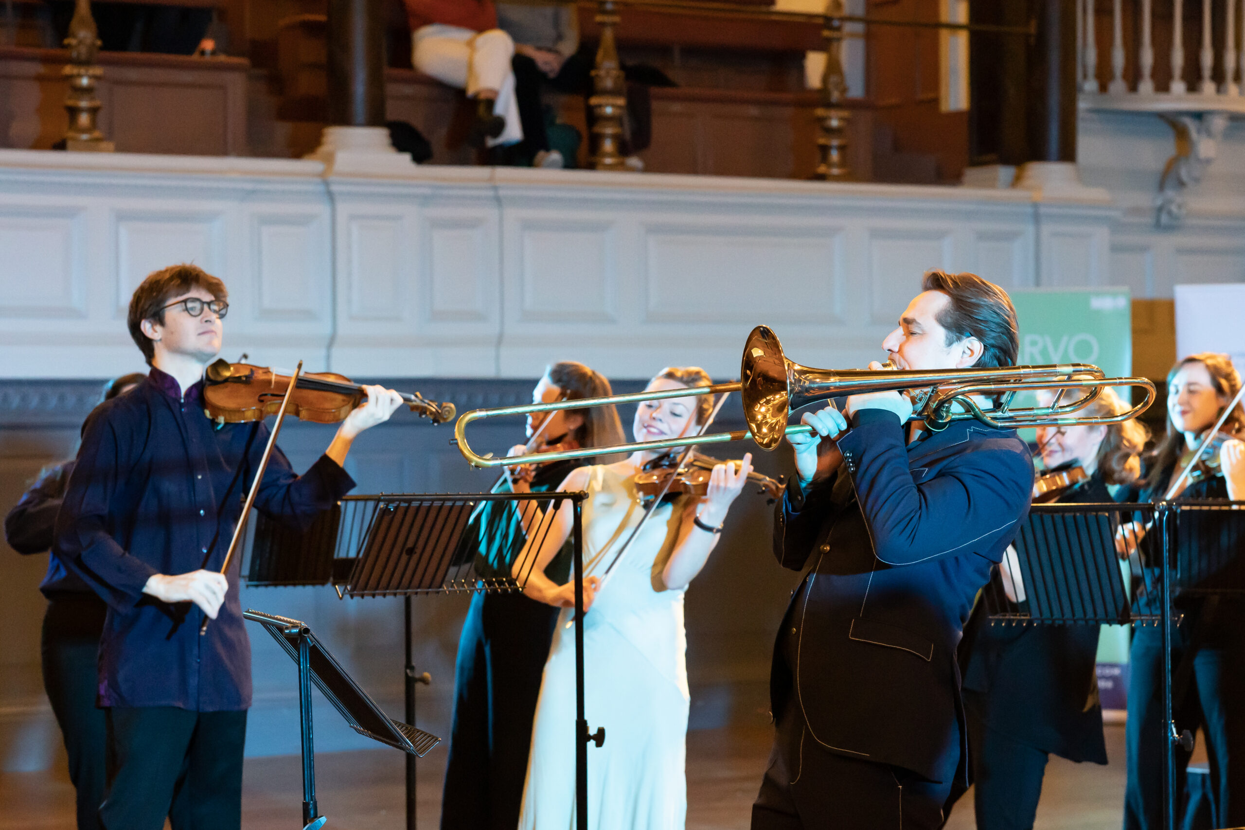 A man plays the trombone with a group of violinists on stage.