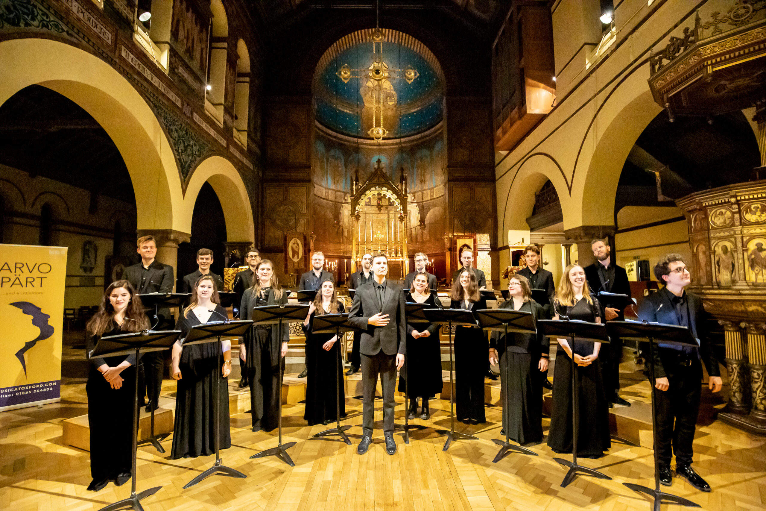 A choir and their director stand in front of the alter of a decorated church.