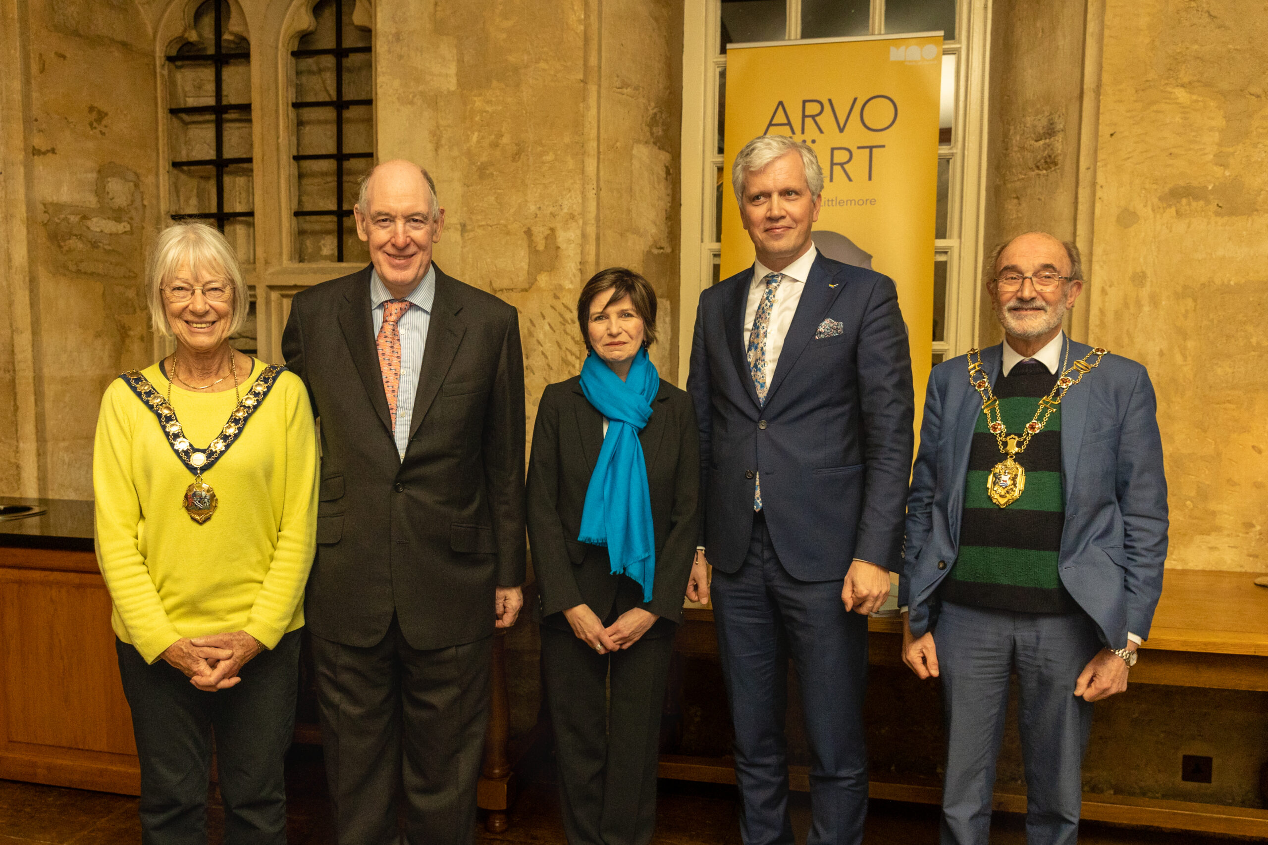 Two women and three men standing in front of a yellow ARVO PÄRT...and a Littlemore festival banner. Two wear chains of office.