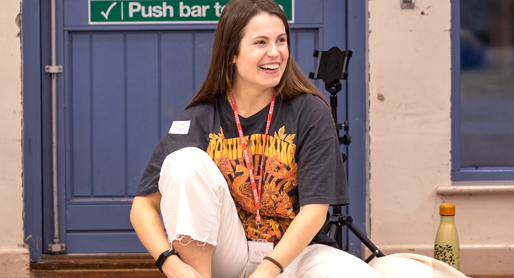 A woman sitting on the floor in a hall with a name badge, laughing