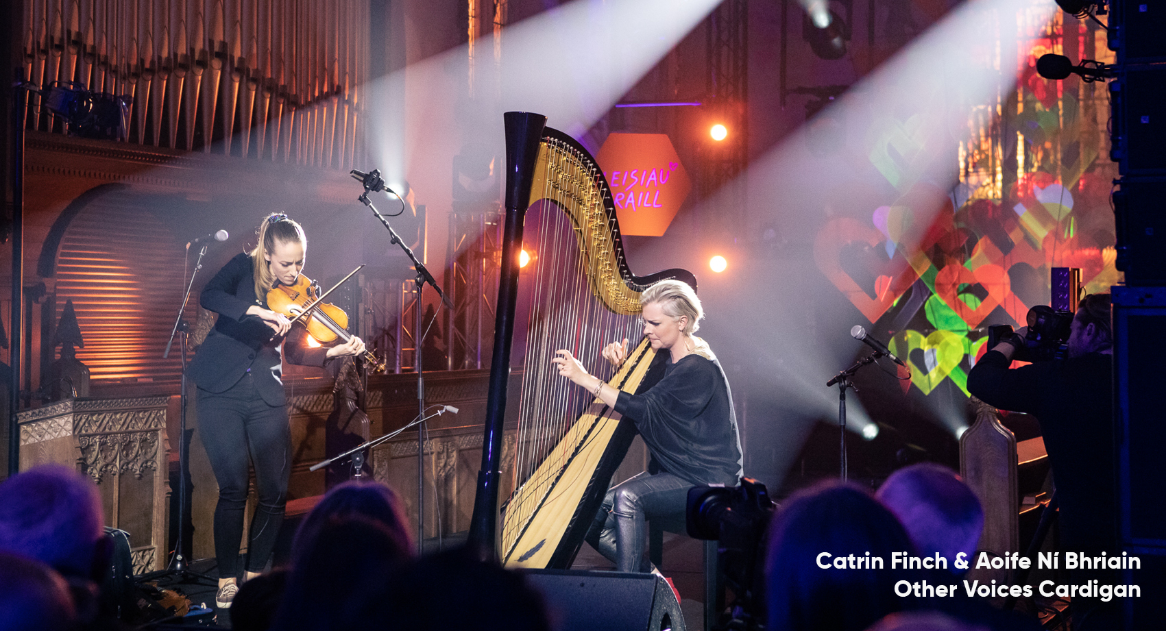 Catrin Finch playing the harp and Aoife Ní Brihain playing the violin under spotlights at Other Voices in Cardigan