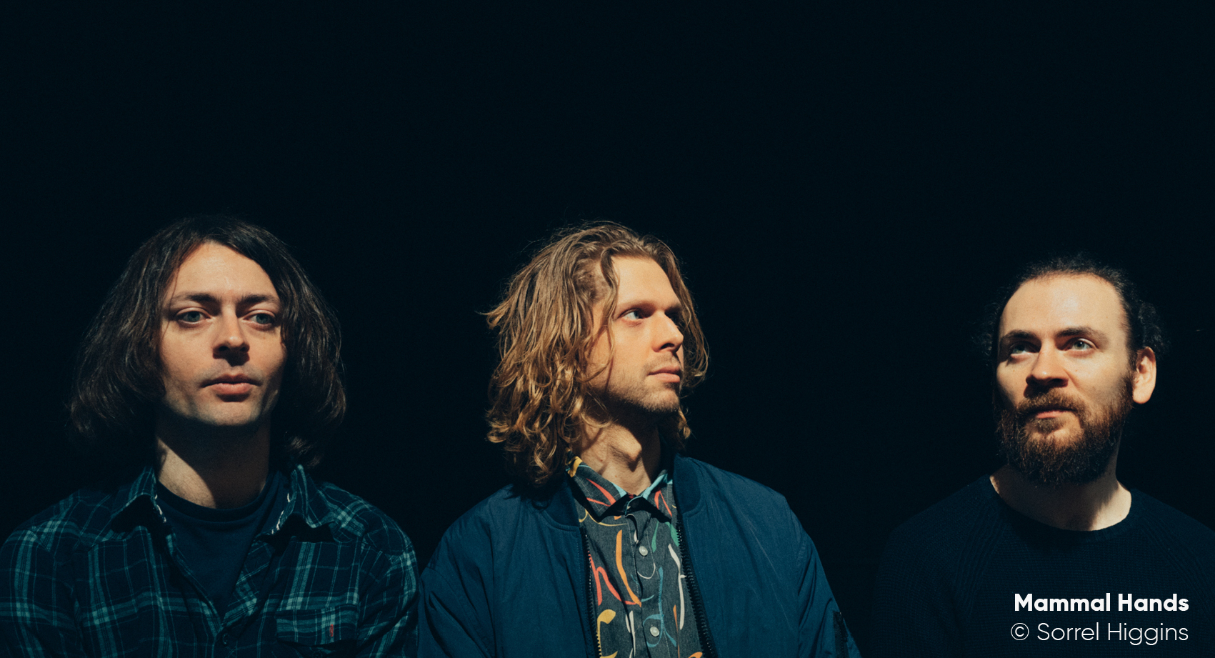 The three members of Mammal Hands standing against a black background.