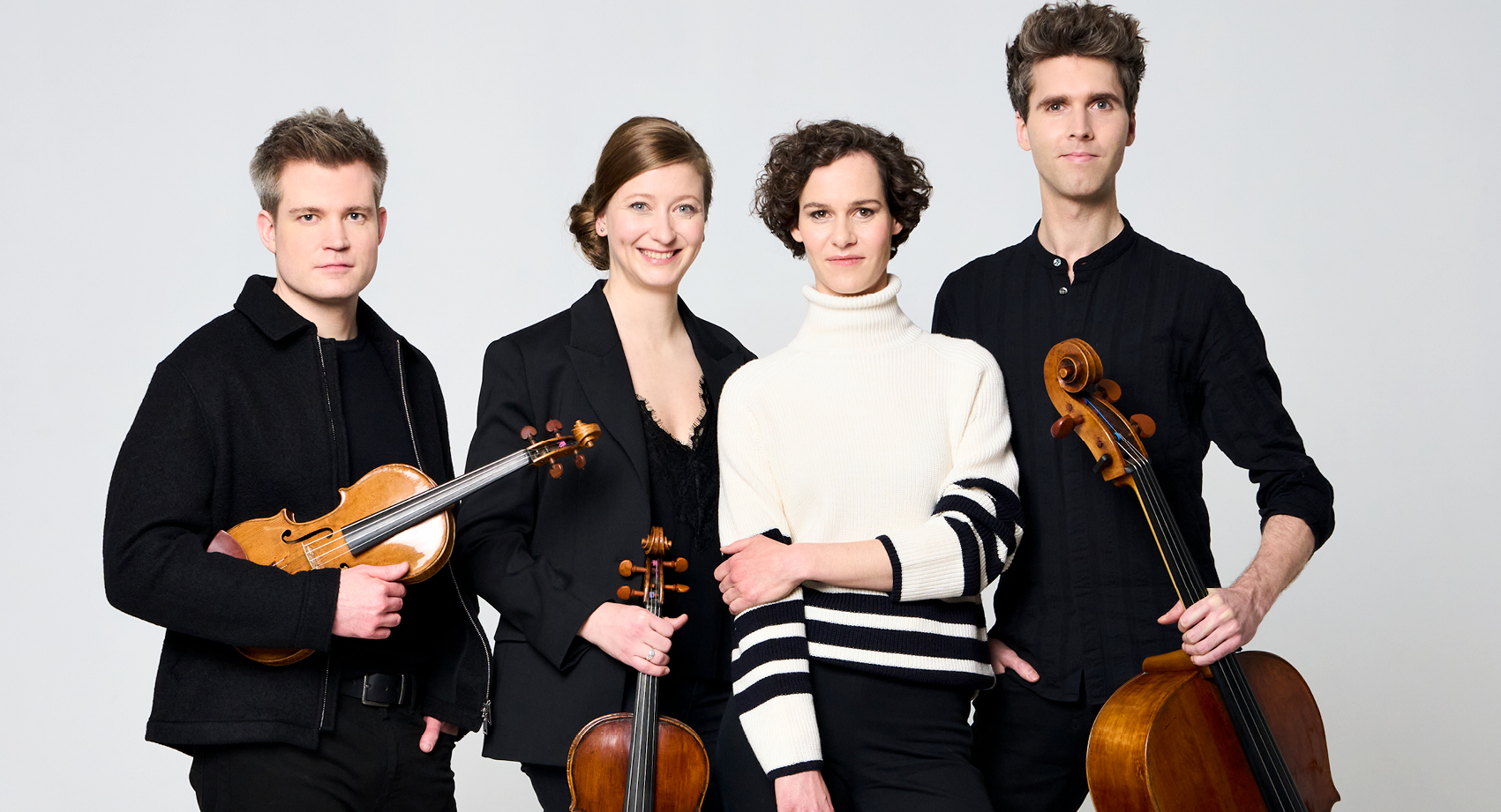 The Notos Quartet dressed in black standing close together. Three are holding instruments, a violin, viola and cello.