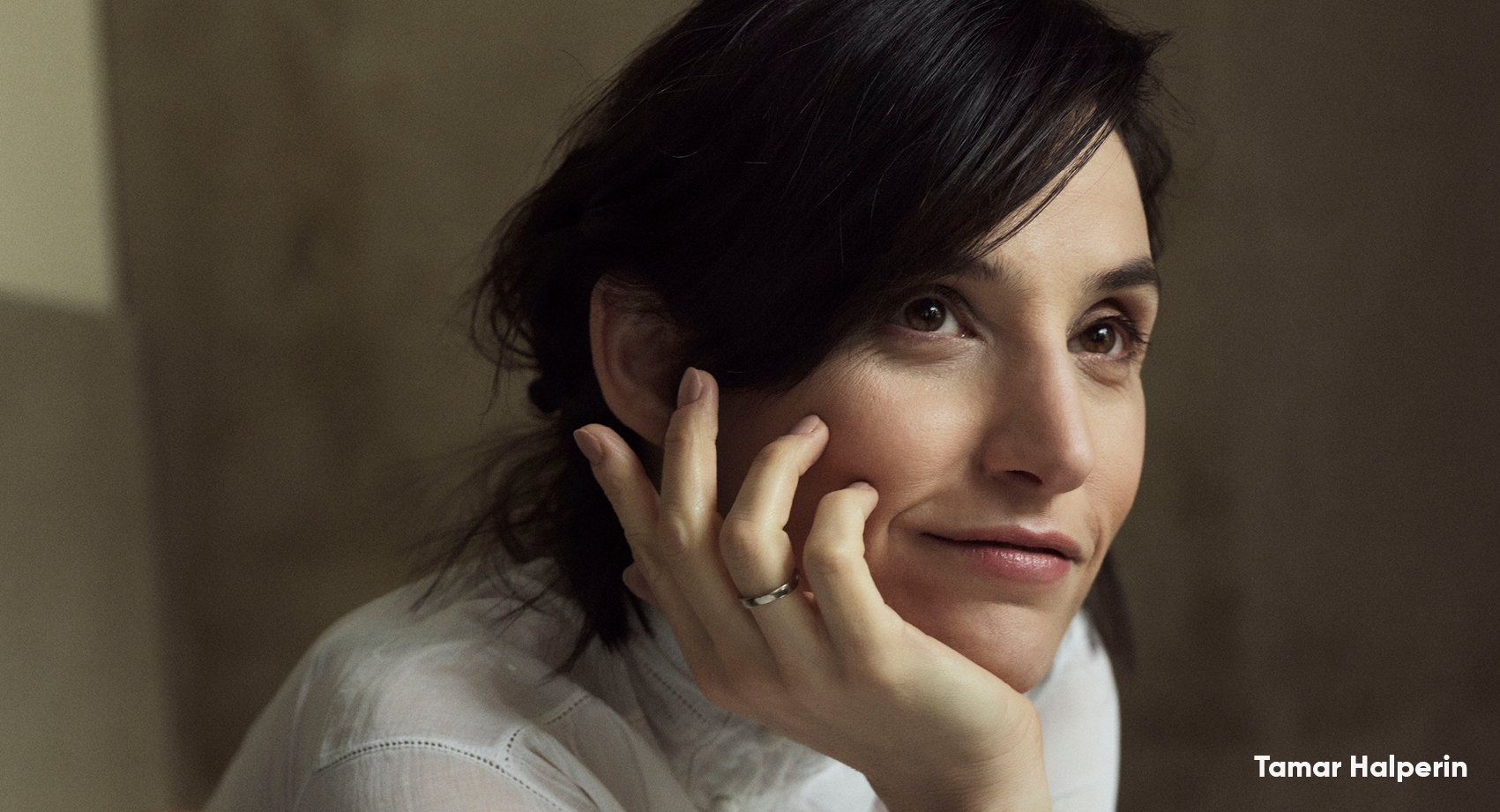 A headshot of Tamar Halperin smiling with her head in her hand, wearing a white top.